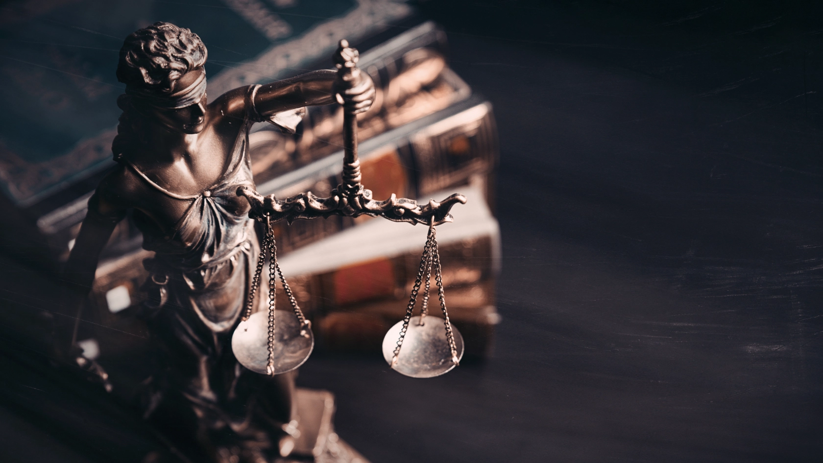 Eine Statue von Justizia steht vor einem unscharfen Bücherstapel im Hintergrund