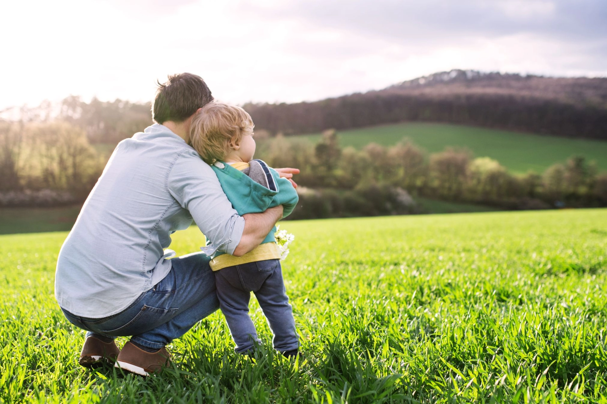 ein Vater schaut mit seinem Kind über eine grüne Landschaft