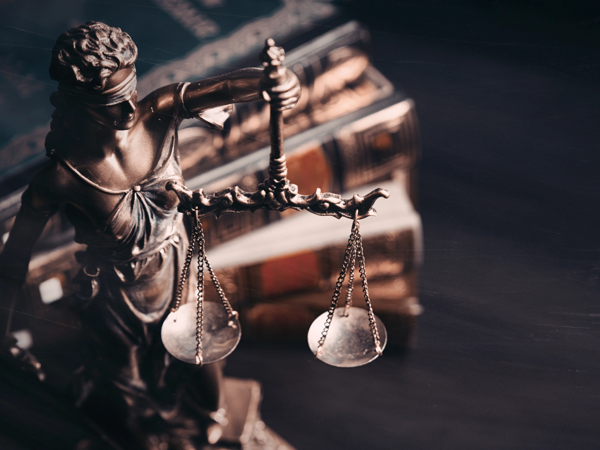 Eine Statue von Justizia steht vor einem unscharfen Bücherstapel im Hintergrund