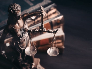Eine Statue von Justizia steht vor einem unscharfen Bücherstapel im Hintergrund